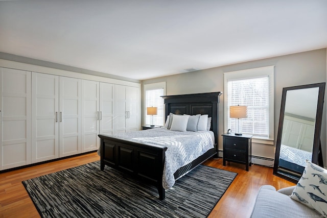 bedroom with hardwood / wood-style floors, a baseboard radiator, and multiple windows