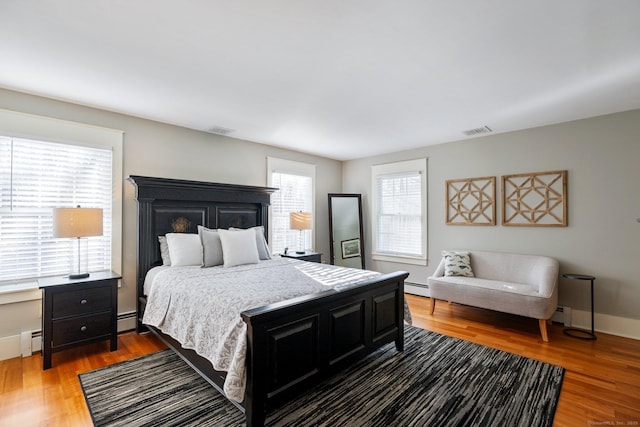 bedroom with wood-type flooring, a baseboard radiator, and multiple windows