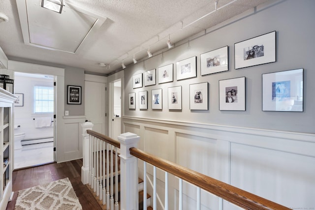 hallway with rail lighting, dark wood-type flooring, a textured ceiling, and a baseboard heating unit