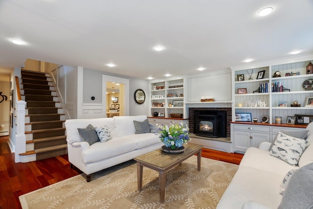 living room featuring built in shelves, hardwood / wood-style flooring, a brick fireplace, and a baseboard heating unit