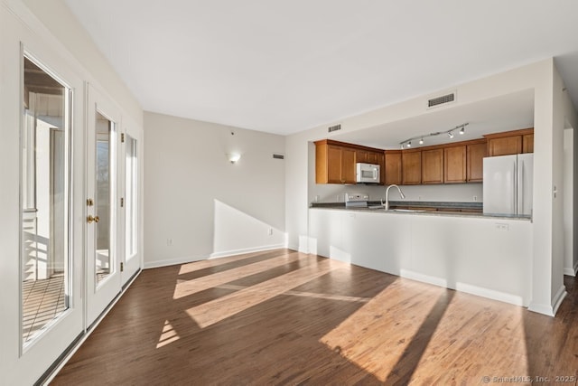 kitchen featuring kitchen peninsula, white appliances, track lighting, and dark wood-type flooring