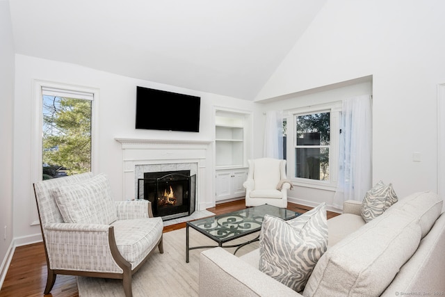 living room featuring a premium fireplace, hardwood / wood-style floors, lofted ceiling, and built in shelves