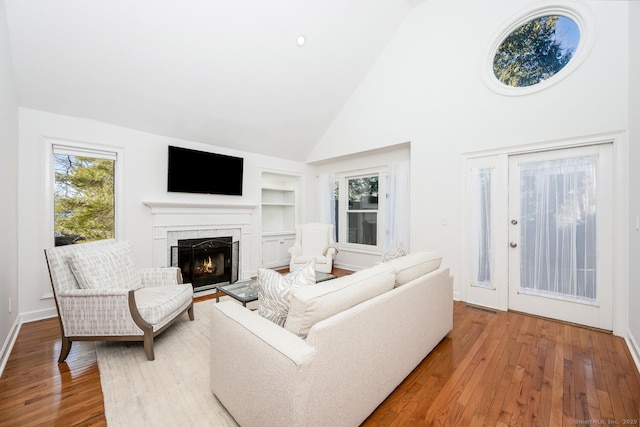 living room with high vaulted ceiling, light wood-type flooring, and built in shelves