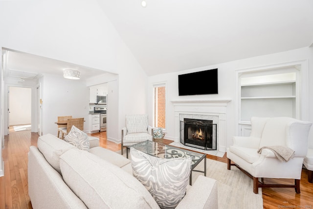 living room with high vaulted ceiling, a premium fireplace, built in shelves, and light hardwood / wood-style floors