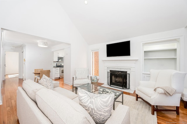 living room featuring a high end fireplace, high vaulted ceiling, light wood-type flooring, and built in shelves