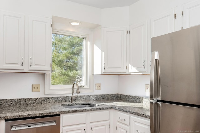 kitchen with stainless steel appliances, dark stone counters, white cabinets, and sink