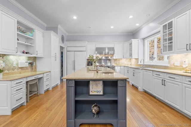 kitchen with extractor fan, white cabinetry, an island with sink, ornamental molding, and light stone counters