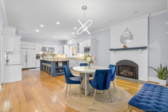 dining area with ornamental molding, a fireplace, a chandelier, and light hardwood / wood-style floors