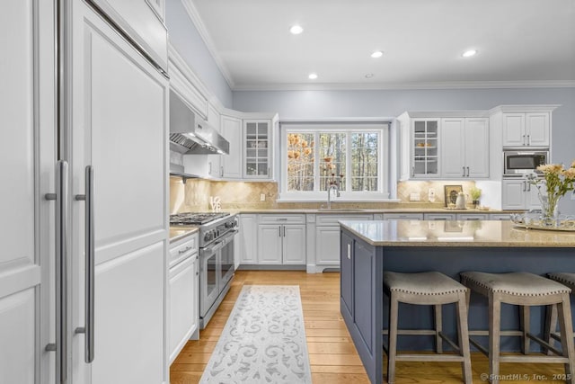 kitchen featuring sink, a breakfast bar area, white cabinets, built in appliances, and light stone countertops