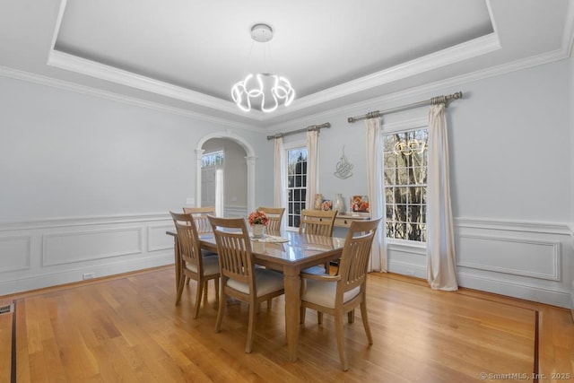 dining room featuring an inviting chandelier, crown molding, a raised ceiling, and light wood-type flooring