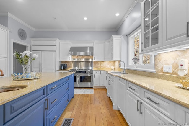 kitchen with blue cabinetry, double oven range, sink, and wall chimney range hood