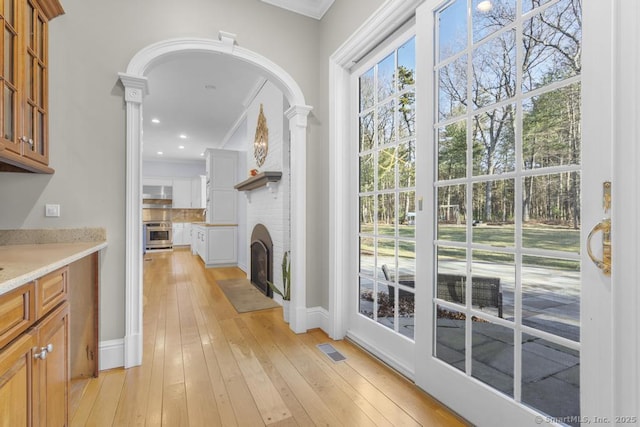 entryway featuring decorative columns, crown molding, a fireplace, and light hardwood / wood-style flooring