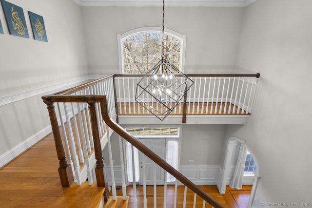 stairway with ornamental molding, a healthy amount of sunlight, hardwood / wood-style floors, and a chandelier