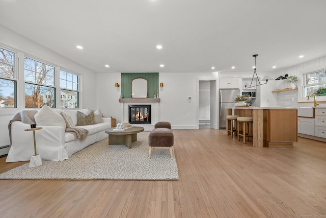 living room with baseboard heating, a fireplace, light hardwood / wood-style flooring, and sink