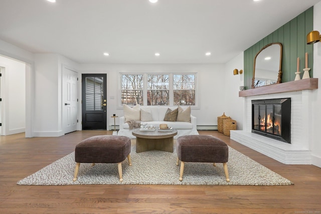 living room with a brick fireplace, wood-type flooring, and a baseboard heating unit