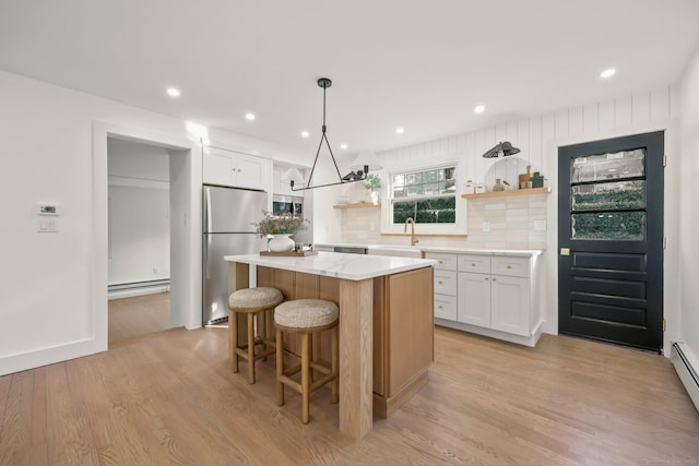 kitchen featuring white cabinetry, stainless steel appliances, a baseboard radiator, a kitchen island, and light wood-type flooring