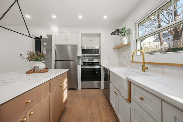 kitchen with backsplash, sink, appliances with stainless steel finishes, light stone counters, and white cabinetry