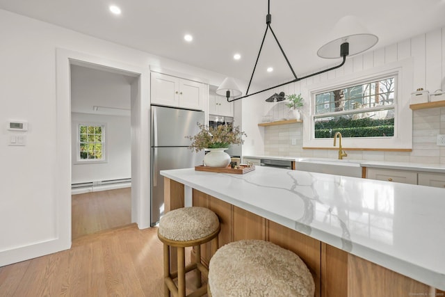 kitchen featuring stainless steel refrigerator, light stone countertops, sink, a baseboard heating unit, and white cabinets