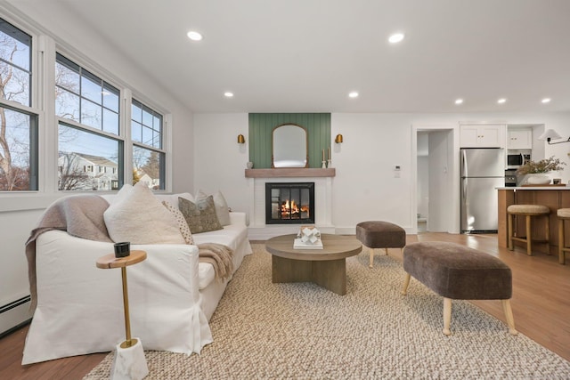 living room featuring a large fireplace, light hardwood / wood-style floors, and baseboard heating