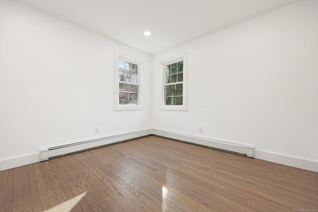 unfurnished room featuring hardwood / wood-style floors and a baseboard heating unit