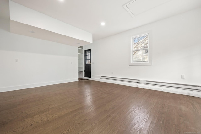 empty room with built in shelves, dark wood-type flooring, and a baseboard radiator