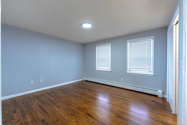 empty room featuring dark hardwood / wood-style flooring and a baseboard heating unit