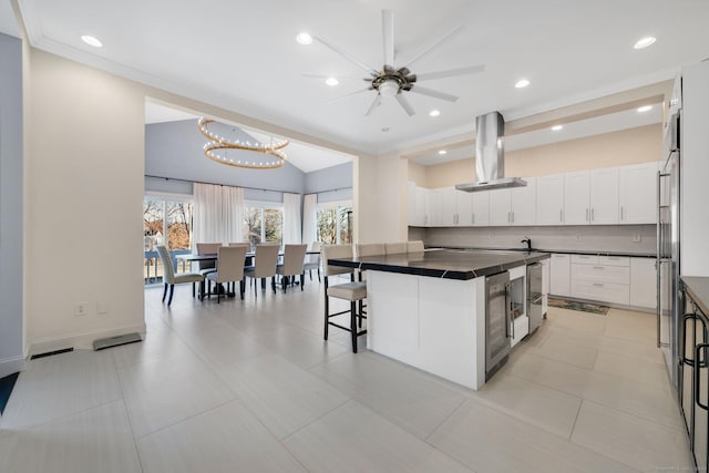 kitchen with a center island, decorative backsplash, a kitchen bar, white cabinetry, and island exhaust hood