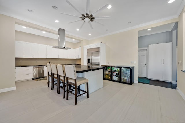 kitchen with appliances with stainless steel finishes, island range hood, white cabinetry, and a breakfast bar area