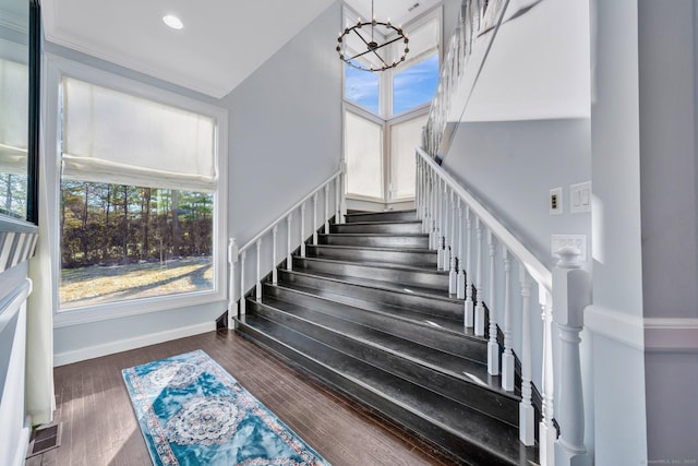 stairs with wood-type flooring, ornamental molding, and an inviting chandelier