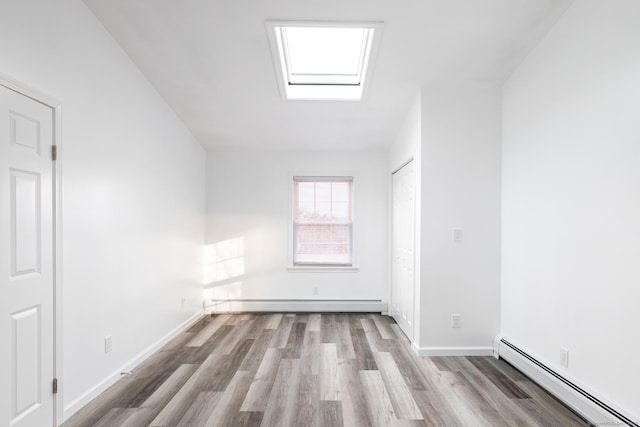 spare room featuring a baseboard heating unit, a skylight, and light wood-type flooring