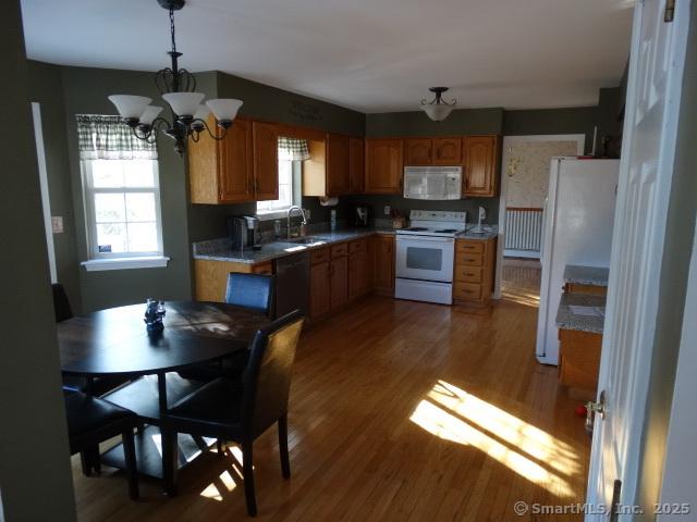 kitchen with white appliances, sink, decorative light fixtures, hardwood / wood-style flooring, and a notable chandelier