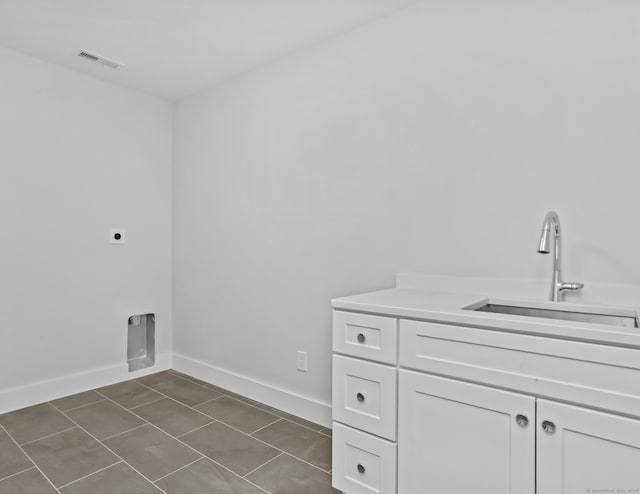 laundry room featuring electric dryer hookup, sink, cabinets, and dark tile patterned flooring