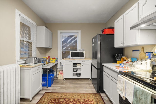 kitchen featuring radiator, stainless steel appliances, white cabinetry, and light wood-type flooring