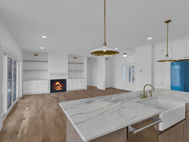 kitchen with light hardwood / wood-style flooring, hanging light fixtures, kitchen peninsula, light stone countertops, and white cabinets