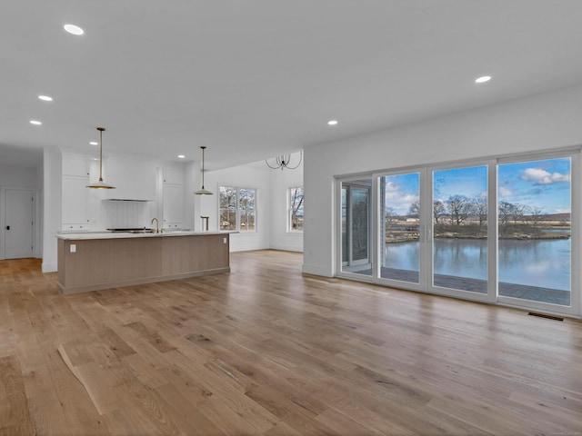 unfurnished living room with sink, a chandelier, and light wood-type flooring