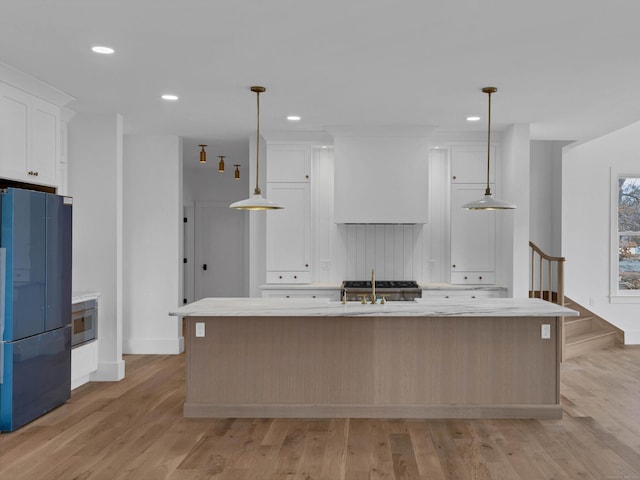 kitchen with black refrigerator, decorative light fixtures, an island with sink, and white cabinets