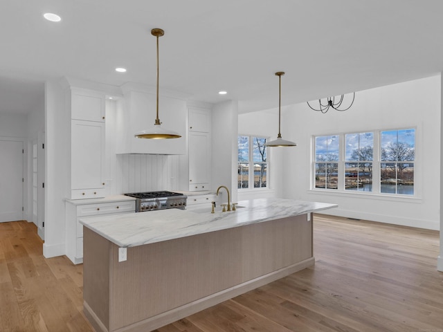 kitchen with pendant lighting, sink, white cabinets, and a center island with sink