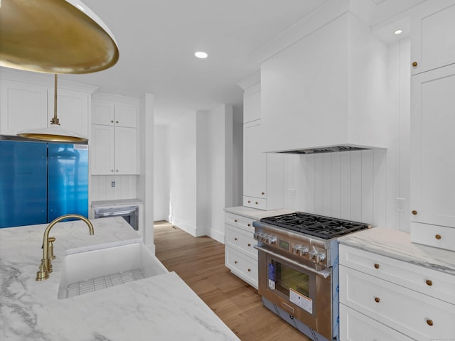 kitchen featuring high end stainless steel range oven, white cabinetry, light stone counters, and refrigerator