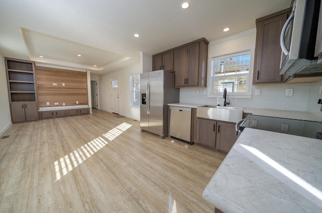 kitchen featuring appliances with stainless steel finishes, backsplash, a raised ceiling, sink, and light hardwood / wood-style floors