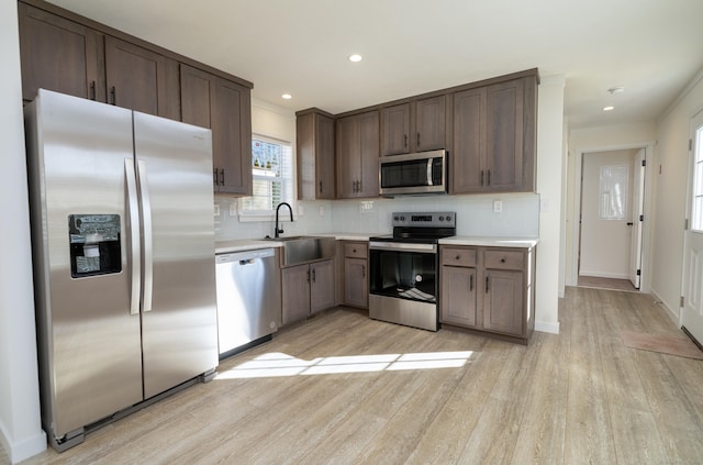 kitchen with dark brown cabinetry, sink, tasteful backsplash, light hardwood / wood-style floors, and appliances with stainless steel finishes