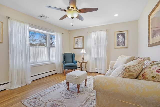 living room featuring baseboard heating, a ceiling fan, visible vents, and wood finished floors