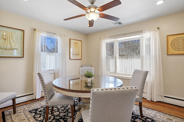 dining space featuring visible vents, wood finished floors, a ceiling fan, and a baseboard radiator