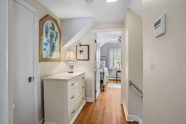 hallway featuring baseboards, lofted ceiling, an upstairs landing, light wood-style floors, and a baseboard radiator