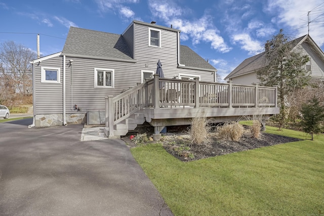 rear view of house with a yard, a deck, and roof with shingles