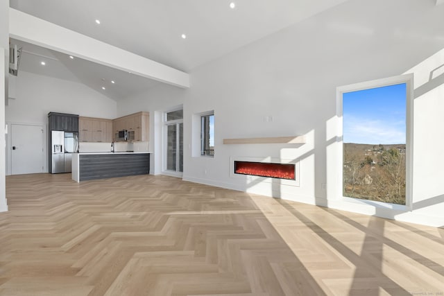 unfurnished living room with plenty of natural light, a towering ceiling, sink, and light parquet flooring