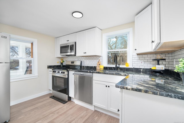 kitchen featuring light hardwood / wood-style flooring, decorative backsplash, white cabinets, appliances with stainless steel finishes, and sink