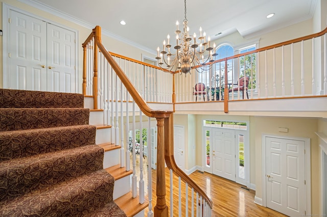 stairway with crown molding, hardwood / wood-style floors, and an inviting chandelier