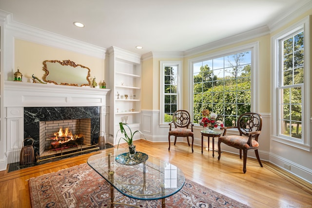 sitting room with light hardwood / wood-style floors, built in features, a fireplace, and ornamental molding