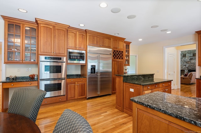 kitchen with built in appliances, light hardwood / wood-style flooring, dark stone countertops, and a fireplace