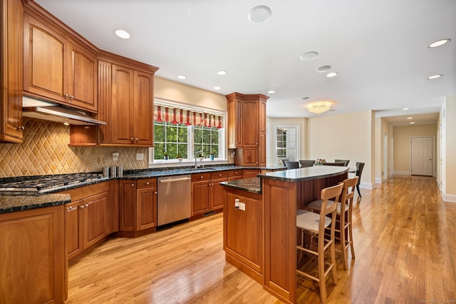 kitchen featuring a kitchen bar, light wood-type flooring, dark stone counters, stainless steel appliances, and a center island